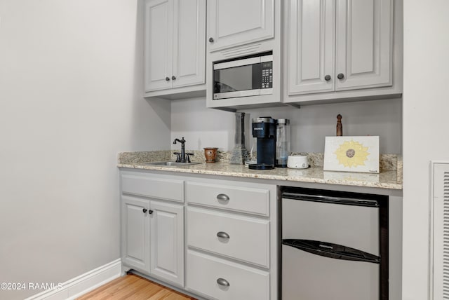 bar with sink, light hardwood / wood-style floors, light stone counters, white cabinetry, and stainless steel appliances