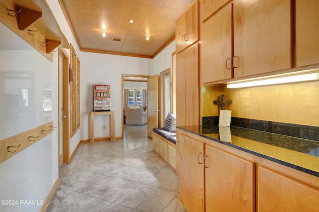 kitchen with dark stone countertops, light brown cabinetry, light tile patterned floors, and ornamental molding