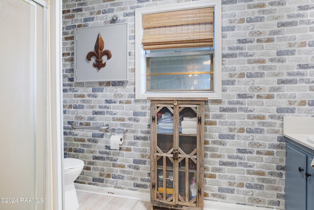 bathroom with vanity, toilet, wood-type flooring, and brick wall