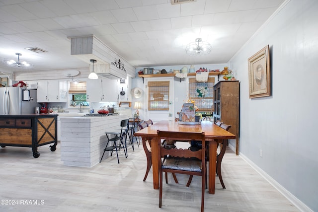 dining area with light wood-type flooring, crown molding, and a notable chandelier