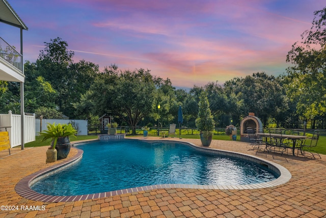 pool at dusk with a patio area and exterior fireplace