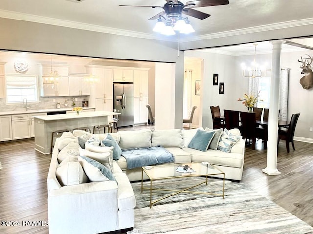 living room with ornate columns, ceiling fan with notable chandelier, crown molding, sink, and hardwood / wood-style floors