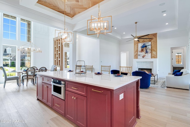 kitchen with a large fireplace, a high ceiling, light wood-style floors, a raised ceiling, and oven