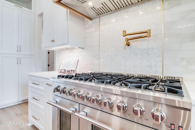 room details featuring white cabinetry, custom exhaust hood, light countertops, decorative backsplash, and range with two ovens