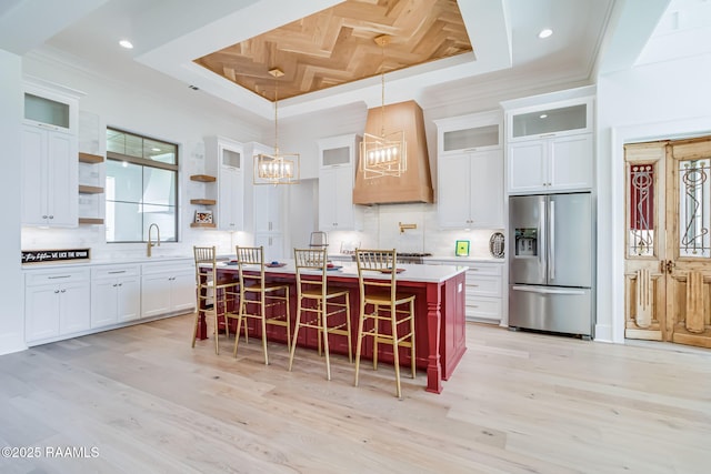 kitchen with stainless steel fridge with ice dispenser, open shelves, premium range hood, a chandelier, and a tray ceiling
