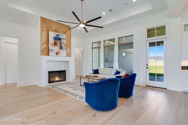 living area with light wood-style floors, ceiling fan, ornamental molding, visible vents, and a premium fireplace