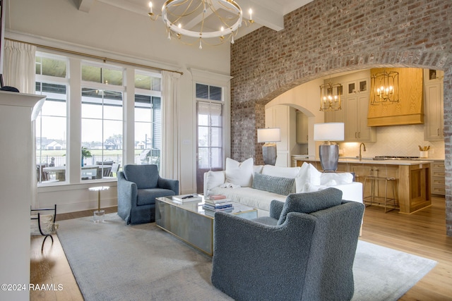 living room featuring beam ceiling, sink, an inviting chandelier, light hardwood / wood-style flooring, and a towering ceiling