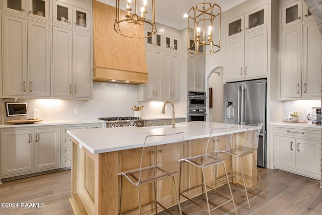 kitchen with an island with sink, a notable chandelier, light hardwood / wood-style floors, light stone counters, and stainless steel appliances