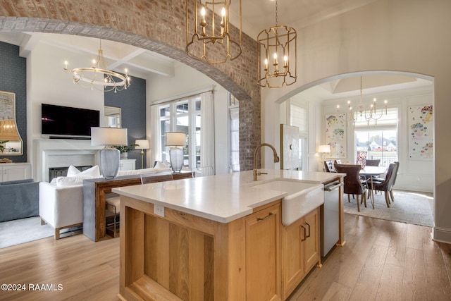 kitchen featuring dishwasher, a kitchen island with sink, sink, light hardwood / wood-style flooring, and decorative light fixtures