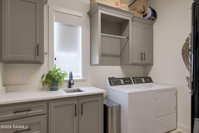 clothes washing area featuring washing machine and dryer, sink, and cabinets