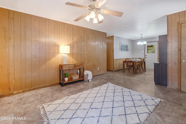 interior space featuring ceiling fan with notable chandelier, concrete floors, and wooden walls