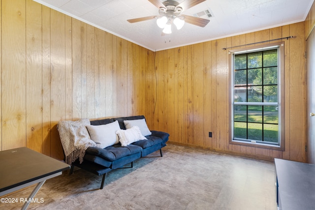 living area with ceiling fan, wood walls, and ornamental molding