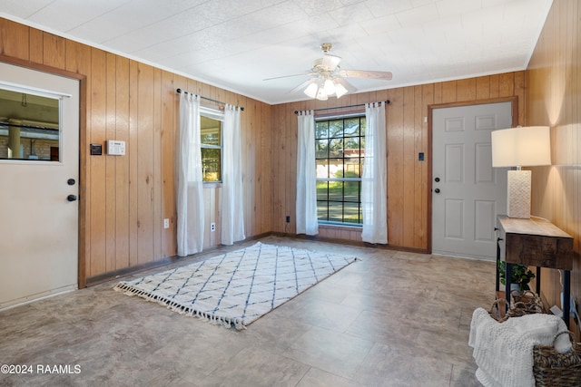 entryway with ceiling fan, wood walls, and ornamental molding