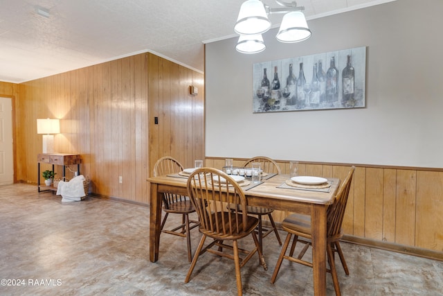 dining room featuring wood walls, ornamental molding, and an inviting chandelier