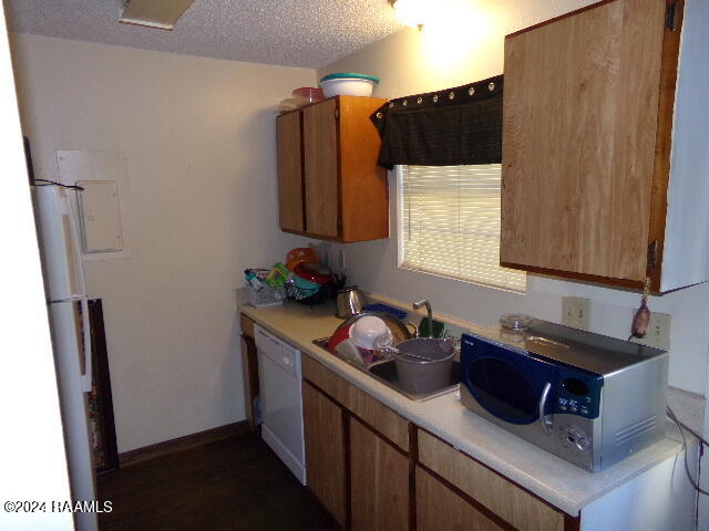 kitchen featuring sink, white appliances, a textured ceiling, and dark wood-type flooring