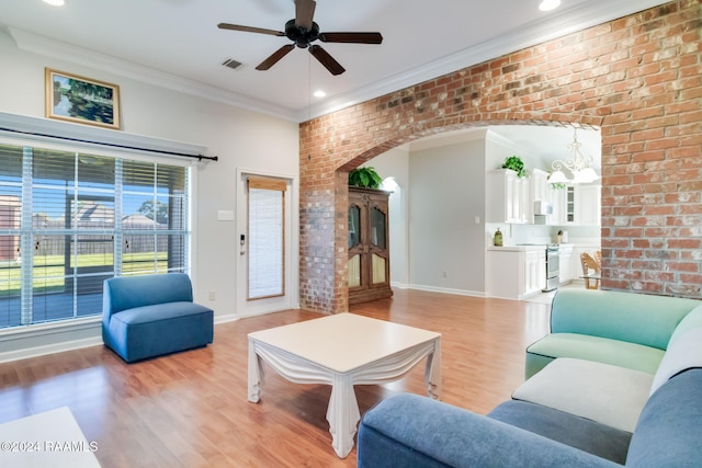 living room with ceiling fan with notable chandelier, light wood-type flooring, ornamental molding, and brick wall