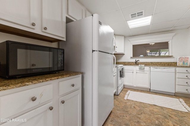 kitchen with a paneled ceiling, dark stone counters, white appliances, sink, and white cabinets