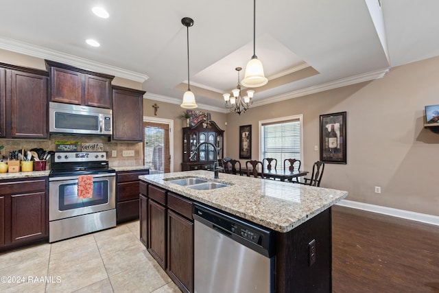 kitchen with sink, appliances with stainless steel finishes, tasteful backsplash, dark brown cabinetry, and an island with sink