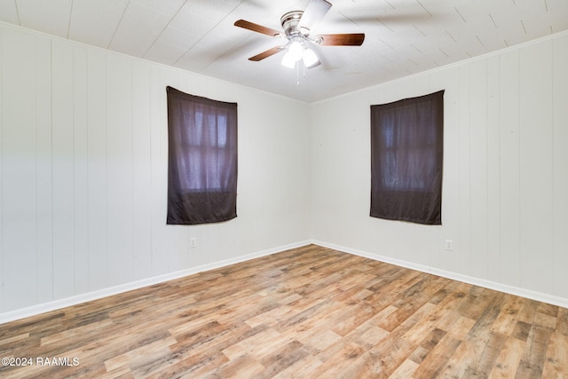 empty room with light hardwood / wood-style floors, crown molding, ceiling fan, and wooden walls