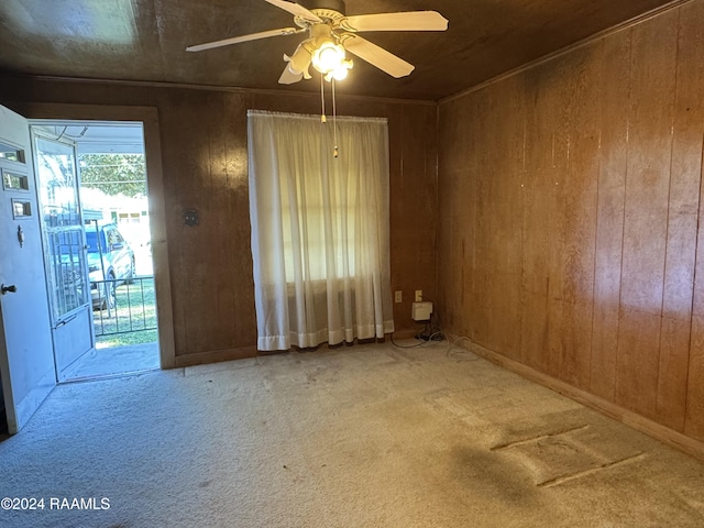 carpeted spare room featuring ceiling fan and wood walls