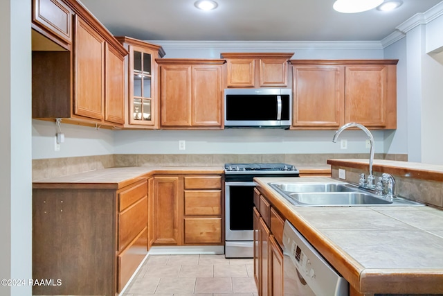 kitchen with sink, ornamental molding, tile counters, light tile patterned flooring, and stainless steel appliances