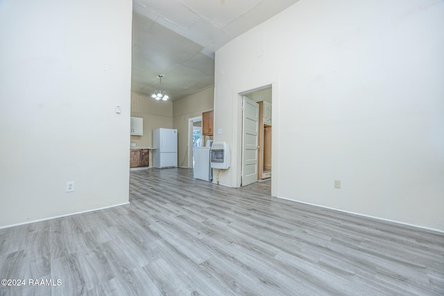 unfurnished living room featuring light hardwood / wood-style flooring, a high ceiling, and an inviting chandelier