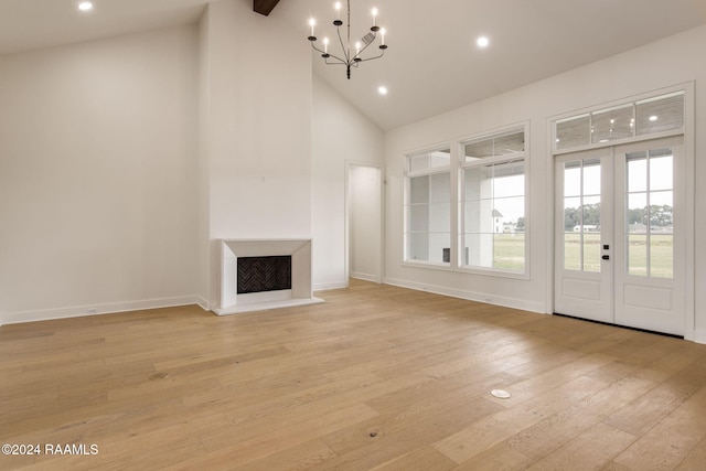 unfurnished living room with french doors, light wood-type flooring, an inviting chandelier, and high vaulted ceiling