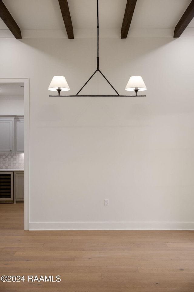 unfurnished dining area featuring beam ceiling, wine cooler, and light hardwood / wood-style floors