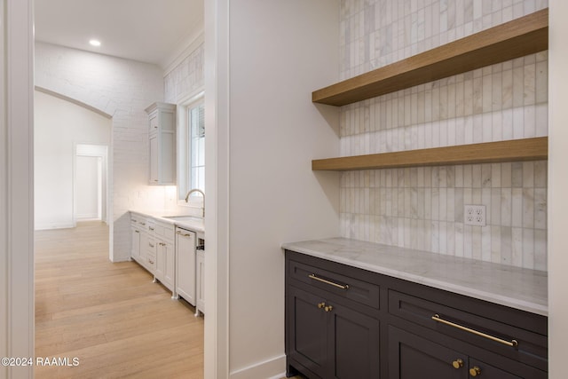 bar with white cabinetry, light stone countertops, light wood-type flooring, and sink