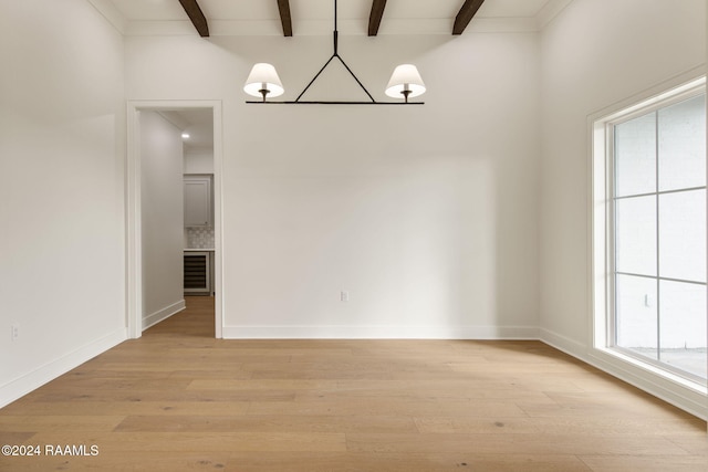 unfurnished dining area featuring beam ceiling, a wealth of natural light, and light wood-type flooring