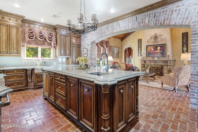 kitchen featuring sink, backsplash, crown molding, pendant lighting, and a kitchen island with sink