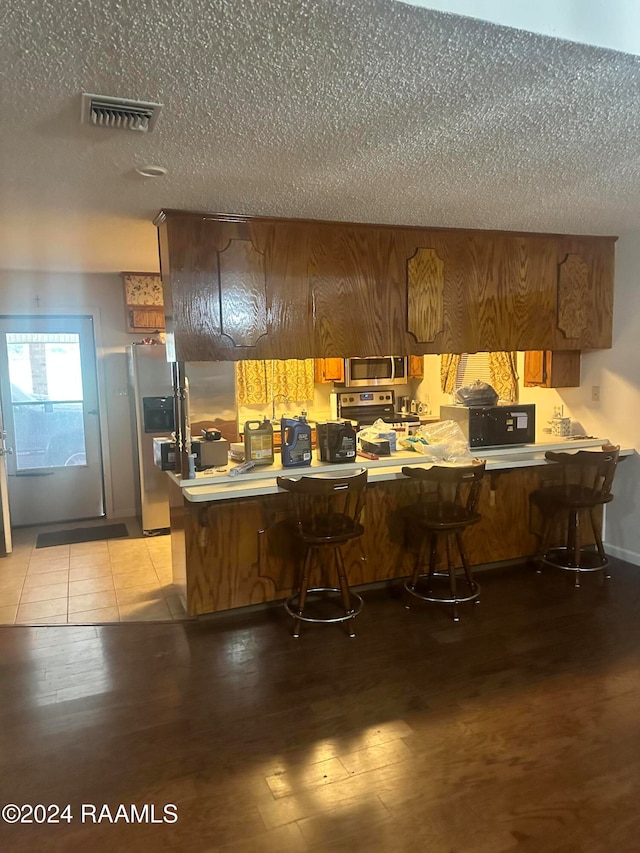 kitchen featuring light hardwood / wood-style floors, kitchen peninsula, a breakfast bar area, and stainless steel appliances