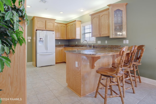 kitchen featuring white refrigerator with ice dispenser, crown molding, light brown cabinetry, kitchen peninsula, and a breakfast bar area