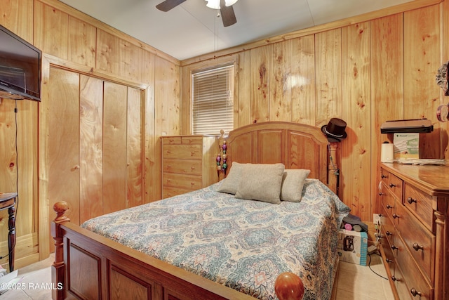 bedroom with ceiling fan, light tile patterned floors, wooden walls, and a closet