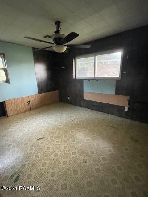 unfurnished room featuring ceiling fan and wood walls