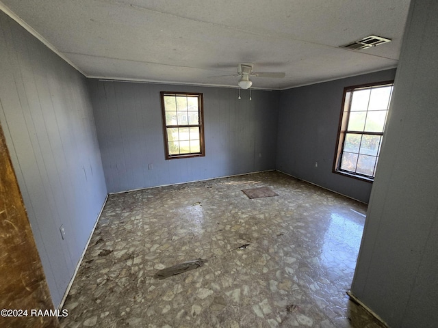 spare room with crown molding, ceiling fan, and wooden walls