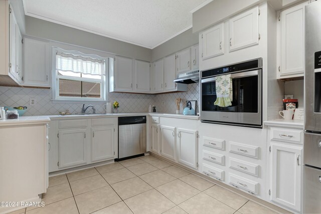 kitchen with appliances with stainless steel finishes, light tile patterned floors, tasteful backsplash, and white cabinetry