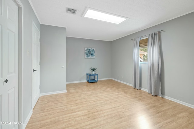 empty room featuring a textured ceiling, light hardwood / wood-style flooring, and ornamental molding