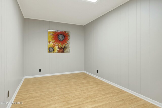 spare room featuring wood walls, ornamental molding, and light wood-type flooring