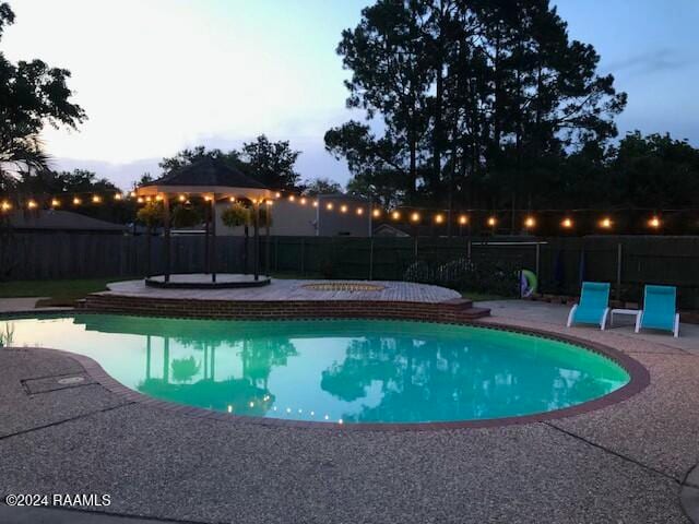 pool at dusk featuring a gazebo and a patio