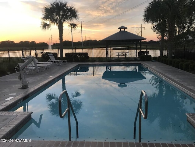 pool at dusk featuring a gazebo, a water view, and a patio