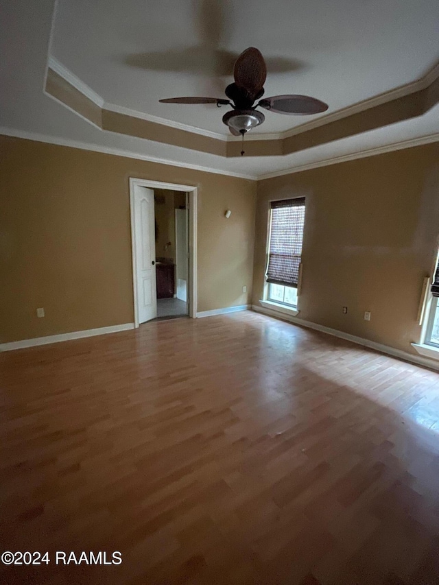 empty room with a tray ceiling, crown molding, hardwood / wood-style floors, and ceiling fan