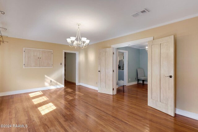 empty room featuring hardwood / wood-style floors, ornamental molding, and an inviting chandelier