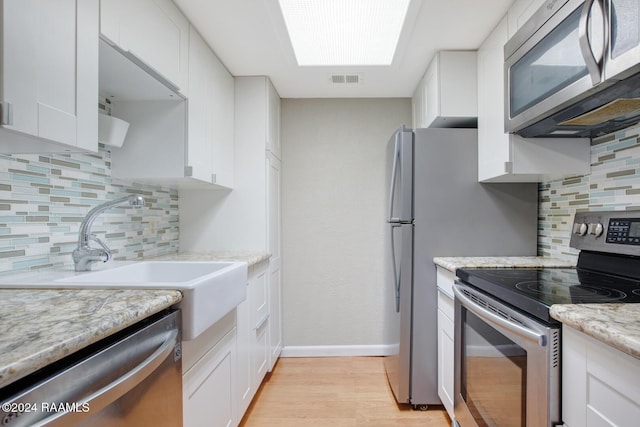 kitchen with white cabinets, backsplash, light hardwood / wood-style floors, and stainless steel appliances