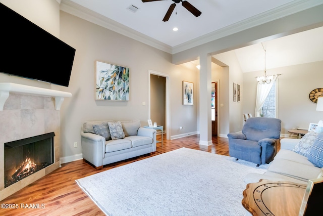 living room featuring lofted ceiling, crown molding, light hardwood / wood-style floors, a tiled fireplace, and ceiling fan with notable chandelier