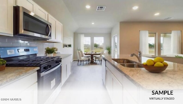 kitchen with sink, stainless steel appliances, light stone counters, backsplash, and white cabinets