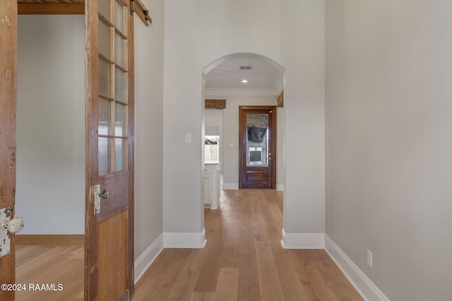 hallway with a barn door, light wood-type flooring, and ornamental molding