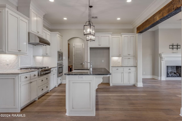 kitchen with appliances with stainless steel finishes, light wood-type flooring, a kitchen island with sink, and dark stone counters