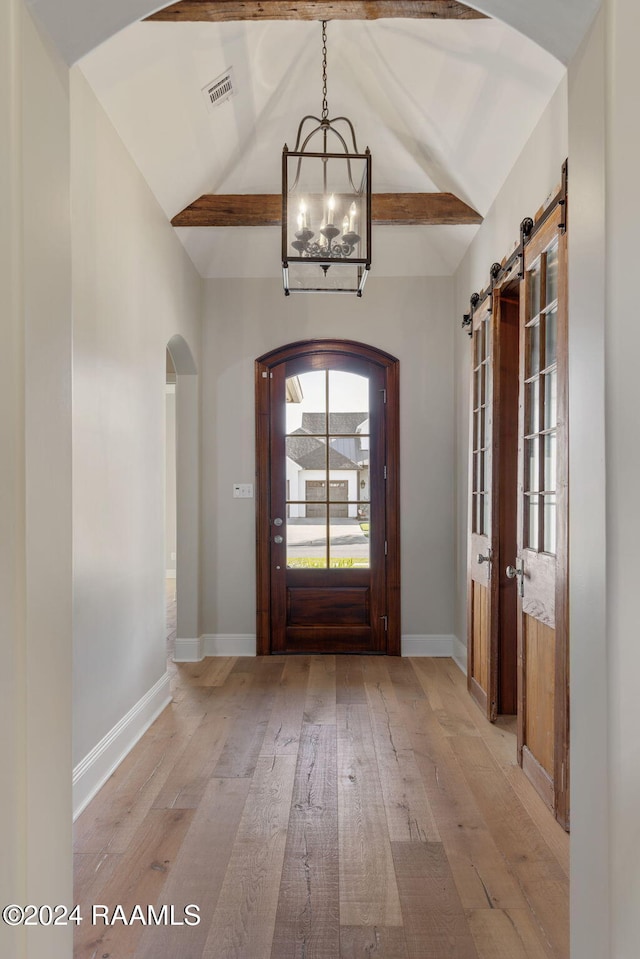 foyer entrance featuring a barn door, lofted ceiling with beams, a notable chandelier, and light hardwood / wood-style floors