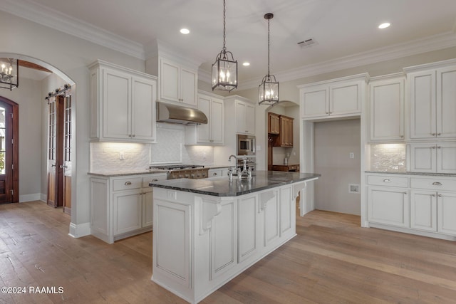 kitchen with white cabinets, light hardwood / wood-style floors, a kitchen island with sink, and appliances with stainless steel finishes